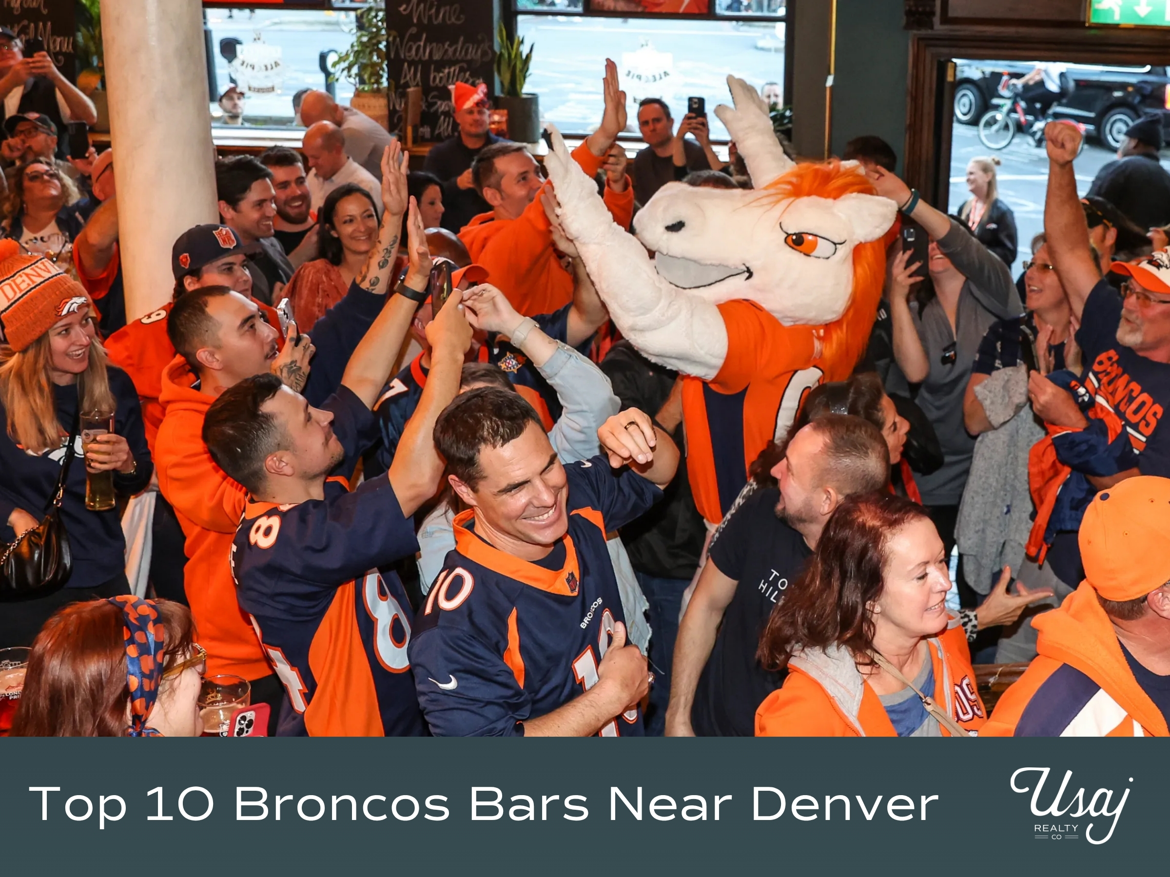 A group of people dressed in Broncos gear celebrate in a bar with a mascot