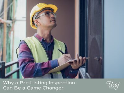 A man in a construction hat and vest holds a clipboard and looks up at a home. Below there is text which says "why a pre-listing inspection can be a game changer" with the Usaj Realty logo.