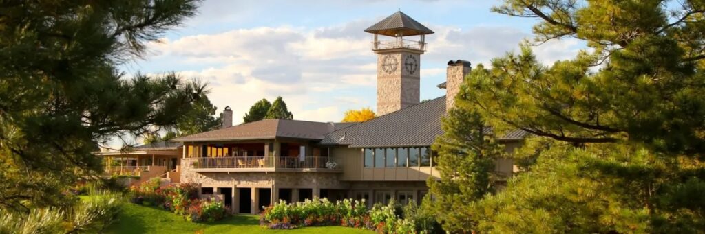 A photo of the exterior of the building that houses the Castle Pines Golf Club. There is a tall clocktower and a covered porch.