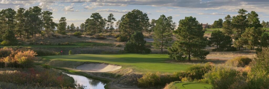 A photo of the Colorado Golf Club course with the green fairway, small pond, and pine trees.