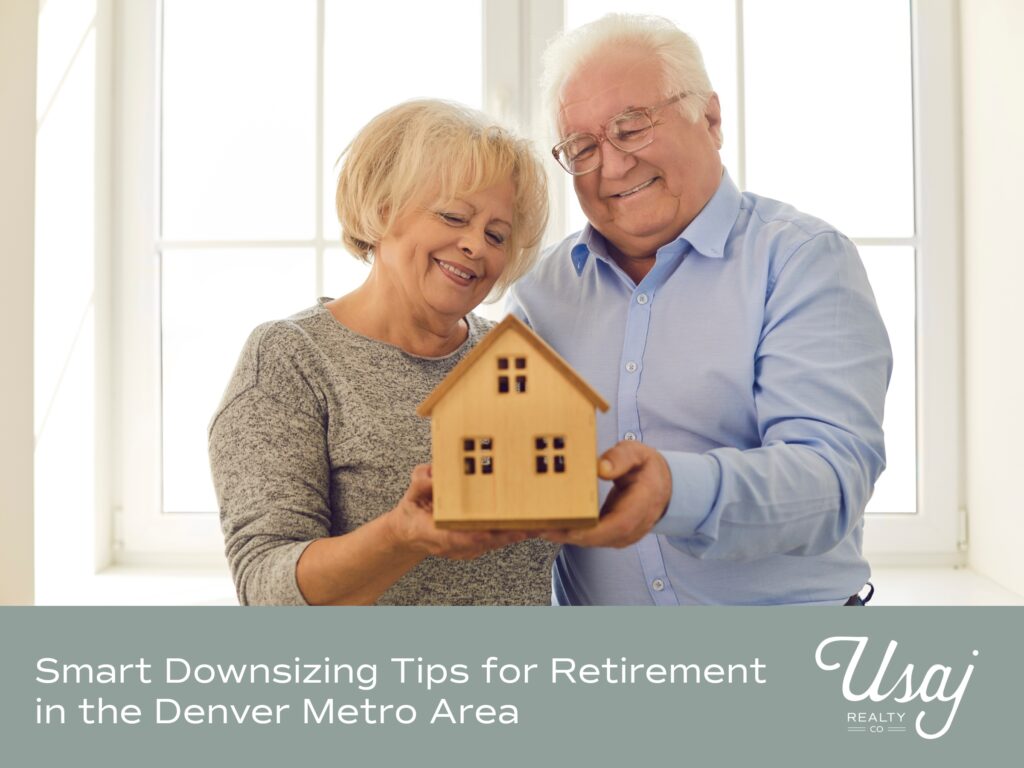 An elderly white couple holds a small wooden house in front of a plain white window. Below the white text and white Usaj Realty logo rest atop a gray background. The text reads: "Smart Downsizing Tips for Retirement in the Denver Metro Area"