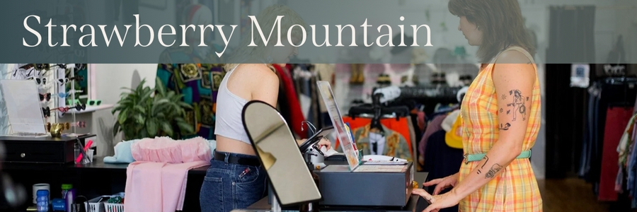 White text over a gray gradient reads, "Strawberry Mountain." Behind the text is a photo of a local secondhand clothing store.